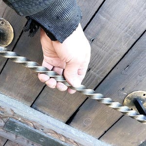 Op de afbeelding: Een gedraaide zwarte metalen deurgreep met gouden accenten. De greep is bevestigd aan een houten deur.