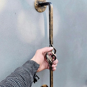 Peut inclure: Une poignée de porte en métal noir avec un design torsadé. La poignée est fixée à un mur avec deux plaques rondes.