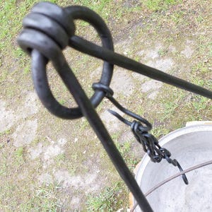 Peut inclure: Un trépied en métal noir avec un crochet et une chaîne pour suspendre une casserole au-dessus d'un feu. Le trépied est en métal robuste et a un aspect rustique.