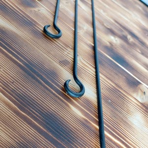 Könnte beinhalten: Vier schwarze Metall-Kaminwerkzeuge mit Haken auf einer Holzoberfläche. Die Werkzeuge sind unterschiedlich lang und in einer Reihe angeordnet.