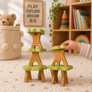 Könnte beinhalten: Holzspielzeug in Form eines Baumes mit grünen und braunen Elementen. Das Spielzeug besteht aus mehreren Teilen, die zu einem Baum gestapelt werden können. Das Bild enthält auch ein gerahmtes Schild mit den Worten "PLAY EXPLORE DREAM BIG".
