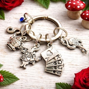 May include: A silver keyring with Alice in Wonderland themed charms. Charms include a teapot, White Rabbit, playing cards, and a flamingo. Red roses and mushroom figurines with white spots surround the keyring.