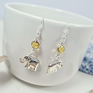 May include: Silver dangle earrings with a small elephant charm and a yellow gemstone.