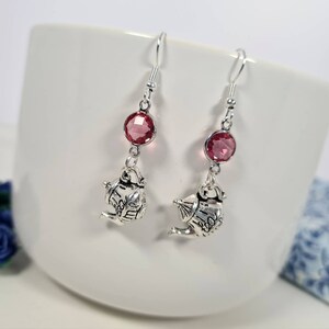 Peut inclure: Boucles d'oreilles pendantes argentées avec un cristal rose et un charme théière.
