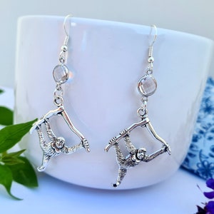 May include: Silver earrings featuring a crystal stone and a monkey hanging from a branch.