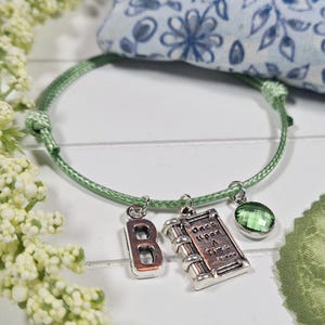 May include: A green cord bracelet with charms, including a book charm that says "Once Upon A Time", a letter "B" charm, and a green crystal charm.