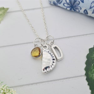 May include: A silver necklace with a charm of a pastry, a letter D charm, and a yellow gemstone.