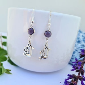 May include: A pair of silver earrings with a purple gemstone and a treble clef charm.