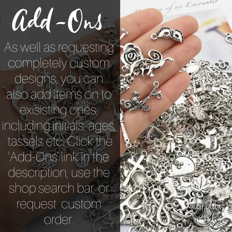 May include: A close-up of a hand holding a variety of silver charms, including a skull, a mask, a bird on a branch, a butterfly, a cross, and a heart. The charms are for adding to jewelry or other crafts. The text 'Add-Ons' is visible in the image.