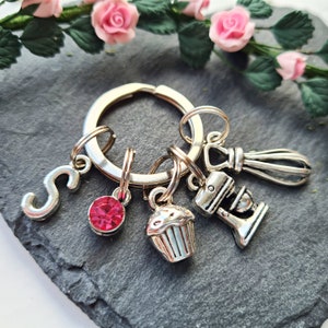 May include: Silver keyring with a pink rhinestone, a cupcake charm, a mixer charm, a whisk charm, and a letter 'S' charm.