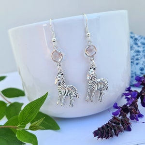 May include: Silver dangle earrings featuring a clear crystal charm and a silver zebra charm.