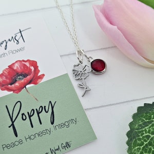Op de afbeelding: Een zilveren ketting met een rode edelsteenhanger en een delicate zilveren klaprooshanger. De ketting wordt getoond op een kaart met de tekst "Augustus Geboortebloem Klaproos Vrede. Eerlijkheid. Integriteit."