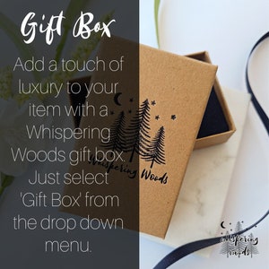 Peut inclure: Une bo&icirc;te cadeau rectangulaire en carton brun avec un tampon &agrave; l'encre noire repr&eacute;sentant trois pins, un croissant de lune et des &eacute;toiles. Le texte Whispering Woods est imprim&eacute; sous les arbres. La bo&icirc;te est ouverte, r&eacute;v&eacute;lant un insert en mousse noire.