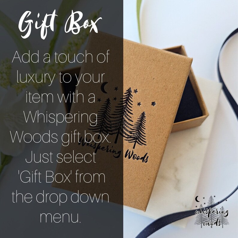 Peut inclure: Une bo&icirc;te cadeau rectangulaire en carton brun avec un tampon &agrave; l'encre noire repr&eacute;sentant trois pins, un croissant de lune et des &eacute;toiles. Le texte Whispering Woods est imprim&eacute; sous les arbres. La bo&icirc;te est ouverte, r&eacute;v&eacute;lant un insert en mousse noire.