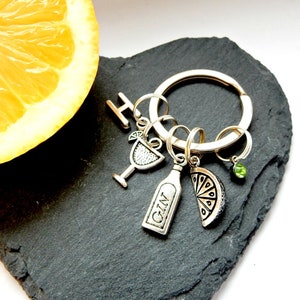 May include: Silver keychain with charms including a martini glass, a bottle with the word "GIN" on it, a lime wedge, and a small green gem.