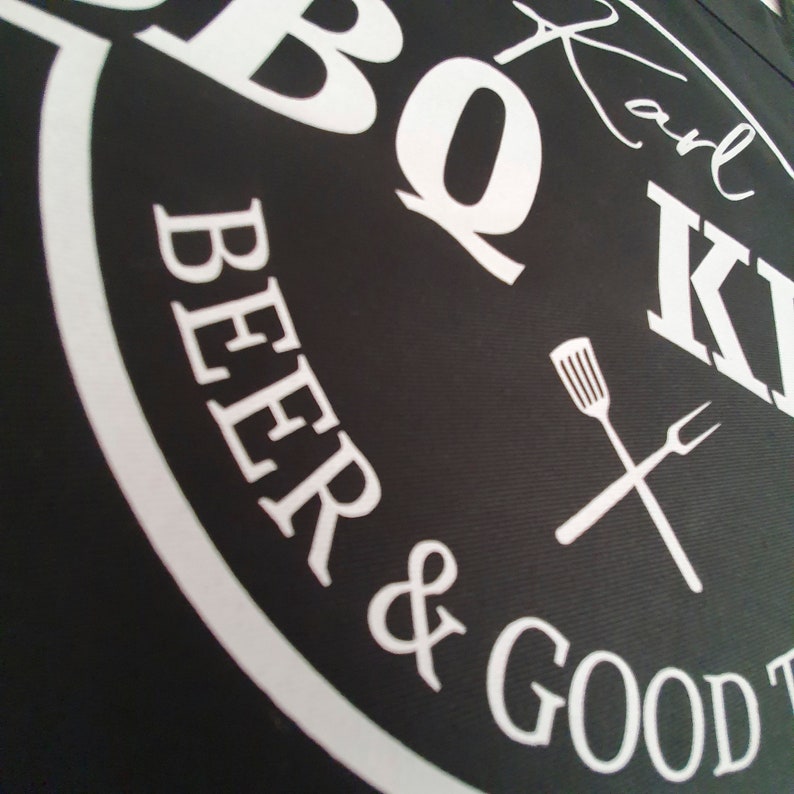 Pu&ograve; includere: Grembiule nero con testo bianco "BBQ Beer & Good Times" e "Karl K". Il design include una spatola e una forchetta incrociate. Il grembiule &egrave; probabilmente per grigliare o cucinare all'aperto.