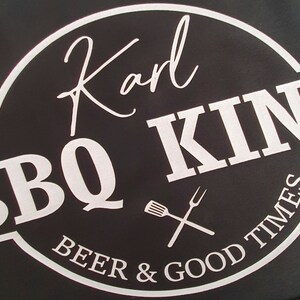 Pu&ograve; includere: Sfondo nero con un logo circolare bianco che recita "Karl BBQ KING" in un font stilizzato. Il logo include una forchetta e una spatola incrociate e le parole "BEER & GOOD TIMES".