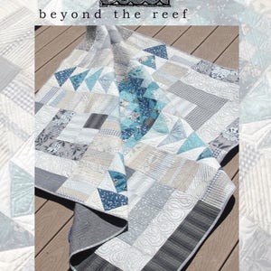 May include: A quilt with a patchwork design featuring a variety of shades of blue, gray, and white. The quilt is folded in half and lying on a wooden surface. The text "beyond the reef homeward" is printed on the image.