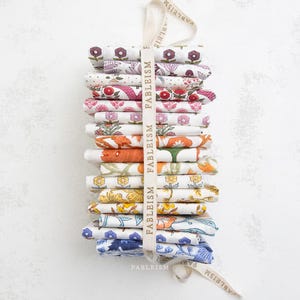May include: A stack of folded fabric squares with floral patterns in various colors, including pink, purple, orange, and blue. The fabrics are tied together with a cream-colored ribbon printed with the word "FABLEISM".