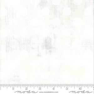 May include: White fabric with a subtle, textured pattern. The fabric has a slightly off-white color and a soft, almost faded look. The fabric is shown with a ruler for scale.