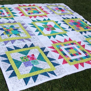 May include: A white quilt with a patchwork design featuring a variety of colors, including pink, green, blue, and yellow. The quilt is made up of squares and triangles, and it has a starburst pattern in the center of each square.