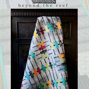 May include: A quilt with a geometric pattern in shades of blue, gray, red, yellow, and green. The quilt is hanging on a dark wooden door. The text "beyond the reef floats" is printed below the quilt.