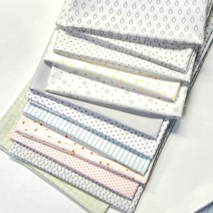May include: A stack of ten white fabric squares with different patterns in gray, black, yellow, and orange. The patterns include polka dots, stripes, geometric shapes, and wavy lines.