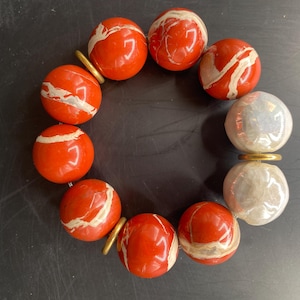 May include: A bracelet made of red and white marbled beads with gold accents and two large white pearl beads.