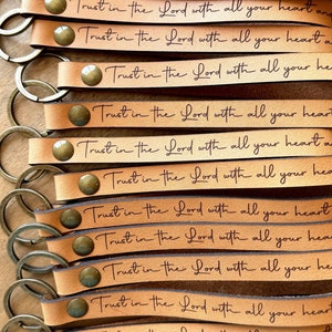 May include: A stack of brown leather keychains with a gold metal ring. Each keychain has the phrase "Trust in the Lord with all your heart and" engraved on it.