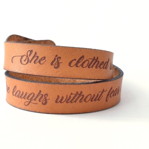 May include: A brown leather wrap bracelet with the words "She is clothed with strength and she laughs without fear" engraved in brown.