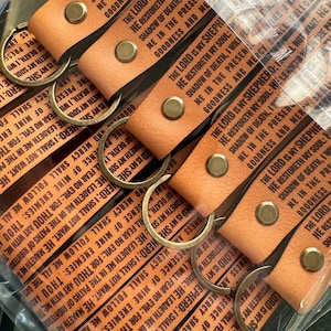 May include: A set of six leather keychains with metal rings. Each keychain features a brown leather strap with black text that reads "The Lord is my Shepherd; I shall not want. He maketh me to lie down in green pastures: he leadeth me beside the still waters. He restoreth my soul: he leadeth me in the paths of righteousness for his name's sake."