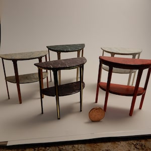 Può includere: Cinque tavolini in miniatura a metà luna con piano in marmo e bordatura dorata. I tavolini sono in legno e hanno una finitura anticata. I tavolini sono disposti in fila su una superficie bianca.