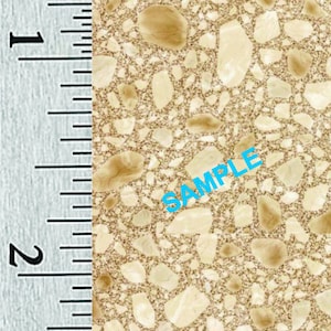 May include: Close-up of a beige and tan speckled surface with the word "SAMPLE" in blue. A ruler on the left shows measurements in inches, with the surface texture resembling a stone or aggregate material.