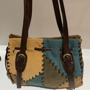 May include: A brown patchwork tote bag with brown leather straps and buckles. The bag is made of different shades of brown, green, and blue fabric.
