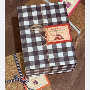 May include: A black and white checkered gift box tied with twine, with a decorative tag that reads "Advent Calendar". Other gift boxes are visible, one with a gold textured pattern and a blue and white checkered ribbon.