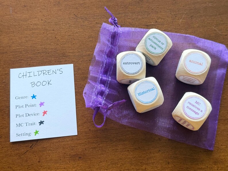May include: A set of wooden dice with words like "extrovert" and "historical" printed on them, along with a card that says "Children's Book". The dice are in a purple drawstring bag.