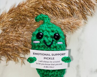 May include: A green crocheted pickle toy holding a sign that says "Emotional Support Pickle. I will always be around to let you know that you are a big dill!"