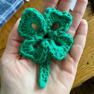 May include: A green crocheted four-leaf clover with a stem.
