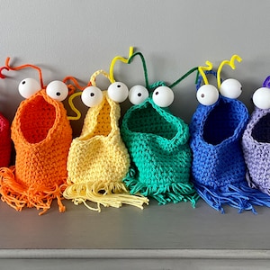 Può includere: Sei cesti appesi all'uncinetto color arcobaleno con occhietti e frange. I cesti sono rosso, arancione, giallo, verde, blu e viola.