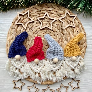 May include: Four handmade gnome ornaments with white yarn beards and crocheted hats in blue, red, gray, and yellow. The gnomes are arranged on a woven straw mat with wooden star cutouts.