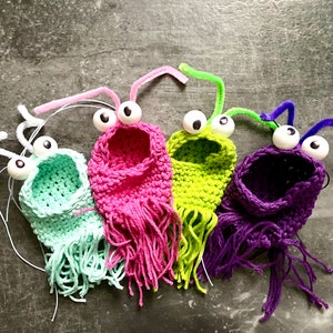 May include: Four crocheted finger puppets with googly eyes and pipe cleaner antennas. The puppets are green, pink, purple, and light blue.