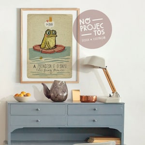 Op de afbeelding: Een ingelijste illustratie van een kikker met een kroon, zittend op een waterlelie. De illustratie heeft de titel "A Princesa e o Sapo" en "The Frog Prince".