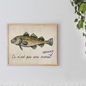 Könnte beinhalten: Eine gerahmte Illustration eines Fisches mit dem Text "PORTUGUAISE" und "Ce n'est pas une morue." Die Illustration ist auf einem beigefarbenen Hintergrund.