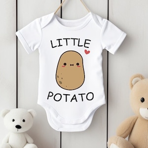 Puede incluir: Un body blanco para bebé con mangas cortas que presenta una patata de dibujos animados con una cara sonriente y el texto "LITTLE POTATO" con un pequeño corazón rojo.