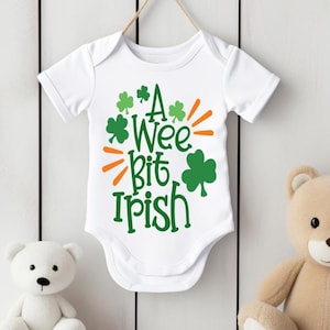 Può includere: Body bianco per neonato con trifogli verdi e dettagli arancioni. Il body dice "A Wee Bit Irish".