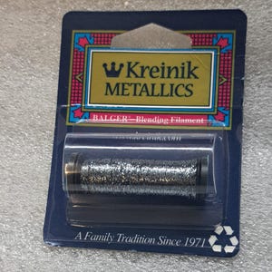 May include: A silver spool of Kreinik Metallics Balger Blending Filament embroidery thread, packaged in a clear plastic blister pack with a blue and gold label that reads "Kreinik Metallics" and "A Family Tradition Since 1971".