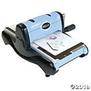 May include: A light blue and black die-cutting machine with a handle on the right side. The machine is on a white surface.