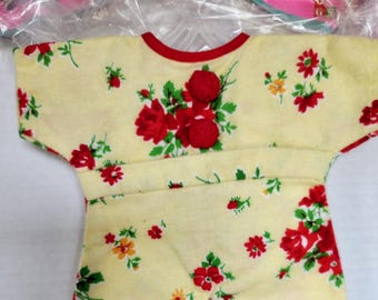 May include: A yellow baby garment with a red trim and floral pattern. The garment features a round neckline and short sleeves. Red pom-poms are used as buttons. The floral pattern includes red and yellow flowers with green leaves.