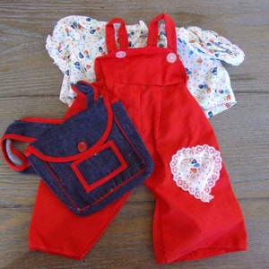 Könnte beinhalten: Ein rotes Latzhosenträger-Outfit mit einem weißen Oberteil mit Blumenmuster und einer blauen Jeans-Tasche. Die Latzhose hat einen herzförmigen Patch auf der Vorderseite.