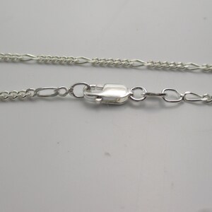 May include: A silver chain necklace with a lobster clasp closure. The chain is a delicate, figaro style.
